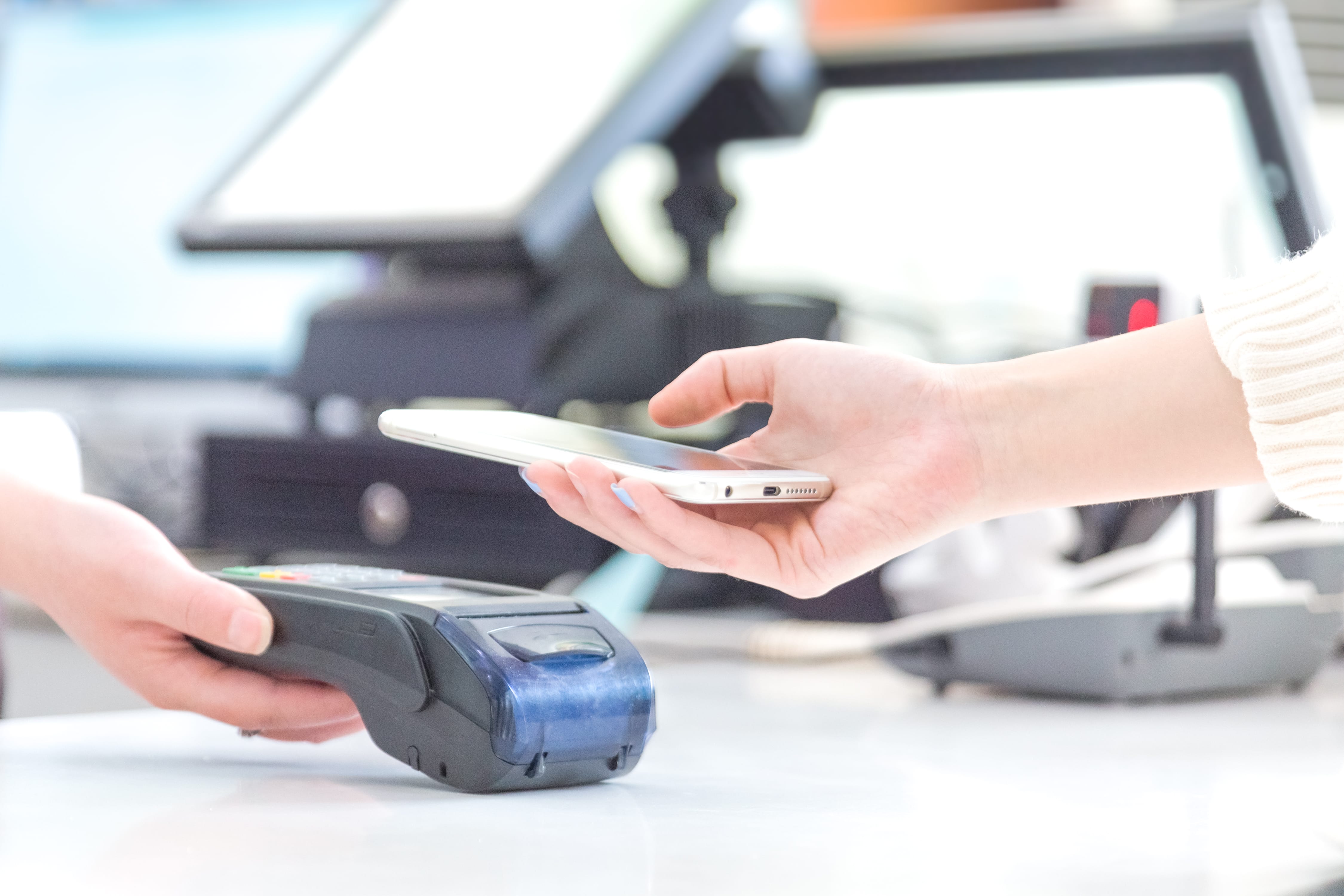 A hand holding a phone over a payments terminal